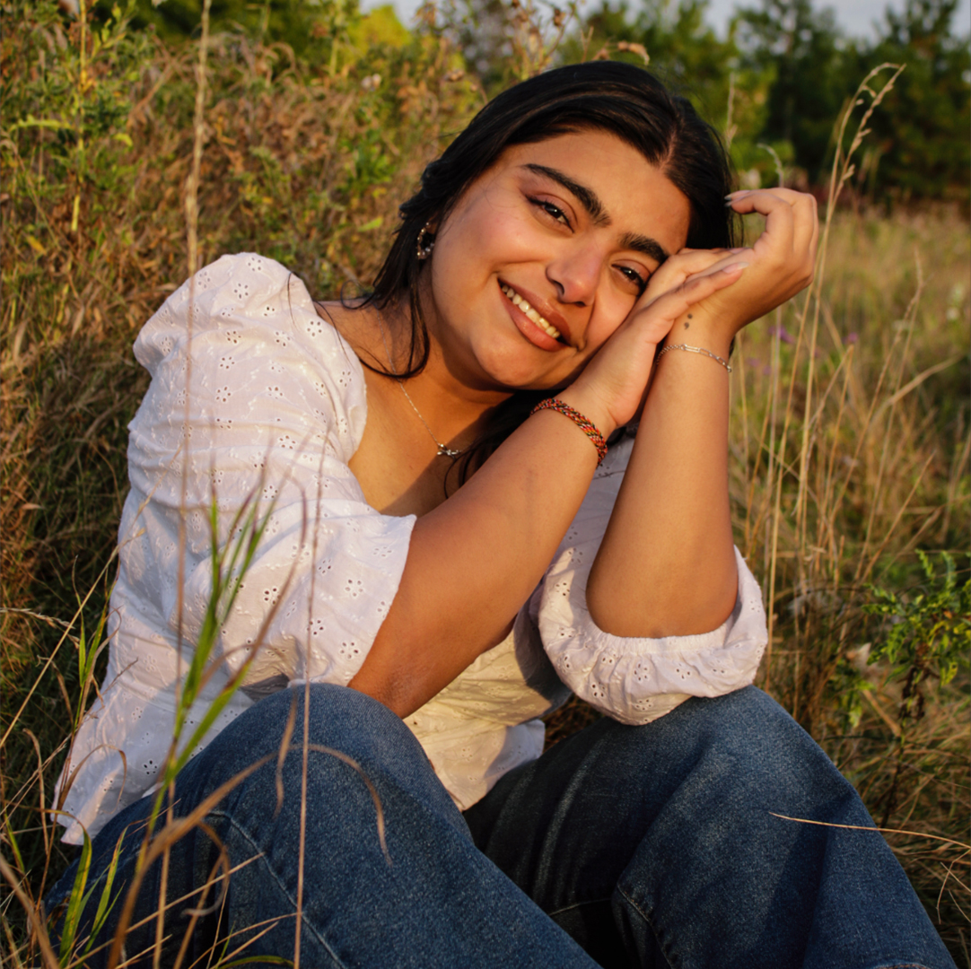 Portrait of a young girl sitting in a grass field smiling at the camera
